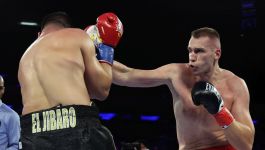 Damian Knyba (fot. Getty Images) Zdjęcie z walki bokserskiej przedstawiające polskiego boksera Damiana Knybę (po prawej), z jasną skórą, w czarnych rękawicach z czerwonymi akcentami i czerwonych spodenkach, wyprowadzającego cios prosty w kierunku tułowia swojego przeciwnika. Przeciwnik Knyby (po lewej), z odsłoniętymi plecami i w czarnych spodenkach z napisem "EL JIBARO" złotymi literami, jest odwrócony plecami i przyjmuje cios. Tło jest ciemne, oświetlone światłami ringu (fot. Getty Images)