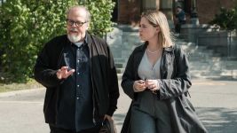 Sophie Lorain i Guy Nadon w serialu  „Projekt niewinność” spacerują obok siebie i rozmawiają. W tle widać kobietę siedzącą na schodach, która rozmawia przez telefon.