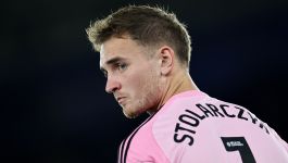 Na zdjęciu widać Jakuba Stolarczyka w różowej koszulce bramkarskiej z czarnymi detalami, stojącego tyłem, lecz z głową zwróconą w bok — jego wyraz twarzy zdradza skupienie i napięcie. Na plecach widnieje wyraźnie nazwisko „STOLARZCZYK” oraz numer „1”, co potwierdza jego rolę jako podstawowego bramkarza. Tuż nad numerem znajduje się logo Sky Bet Championship i EFL, wskazujące na ligowy kontekst fotografii (fot. Getty Images)