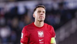 Na zdjęciu Jan Bednarek, kapitan reprezentacji Polski, stoi na murawie w czerwonej koszulce meczowej z orłem na piersi i numerem 5. Żółta opaska kapitańska na jego lewym ramieniu podkreśla jego rolę lidera drużyny. Na koszulce widnieje napis „FINLANDIA–POLSKA 16 CZERWCA 2023”, przypominający o niedawnym spotkaniu międzynarodowym. Tło jest rozmyte, co sugeruje obecność kibiców na stadionie, ale skupia uwagę na zawodniku (fot. Getty Images)