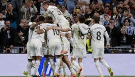 Piłkarze Realu Madryt w białych strojach celebrują gola, obejmując się na boisku. Jeden z zawodników (prawdopodobnie Kylian Mbappe, zdobywca dwóch bramek) jest podniesiony przez kolegów. W tle widać wiwatujących kibiców na trybunach stadionu Santiago Bernabeu. Na plecach jednego z piłkarzy widoczny jest numer "8" (Fede Valverde), a na plecach innego "18" (prawdopodobnie Aurélien Tchouaméni lub inny zawodnik z ty. Ujęcie ukazuje radość drużyny po zdobyciu bramki podczas meczu, w którym pokonali Valencię 3:0.