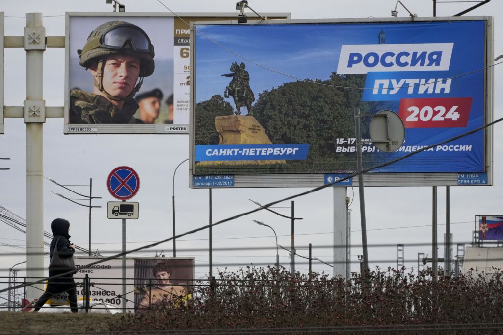 Жанчына праходзіць міма білборда справа, які рэкламуе будучыя прэзідэнцкія выбары, і білборд злева, які прапагандуе кантрактную службу ў расейскай арміі. Санкт-Пецярбург, Расея. 11 сакавіка 2024 года. (Фота: Dmitri Lovetsky / AP Photo / East News)