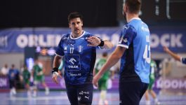 Mężczyzna, piłkarz ręczny Orlen Wisły Płock, stoi na boisku. Ubrany jest w niebiesko-granatową koszulkę w moro z numerem 17 i logo Orlen, z opaskami na nadgarstkach. Ma ciemne włosy, wąsy i spogląda na kolegę z drużyny, stojącego tyłem w podobnej koszulce z numerem 43. W tle widoczni są niewyraźni zawodnicy i bandy reklamowe z napisem "ORLEN". Piłkarze ręczni Wisły Płock pokonali Paris Saint-Germain 35:32 w meczu Ligi Mistrzów. (fot. PAP/Szymon Łabiński)