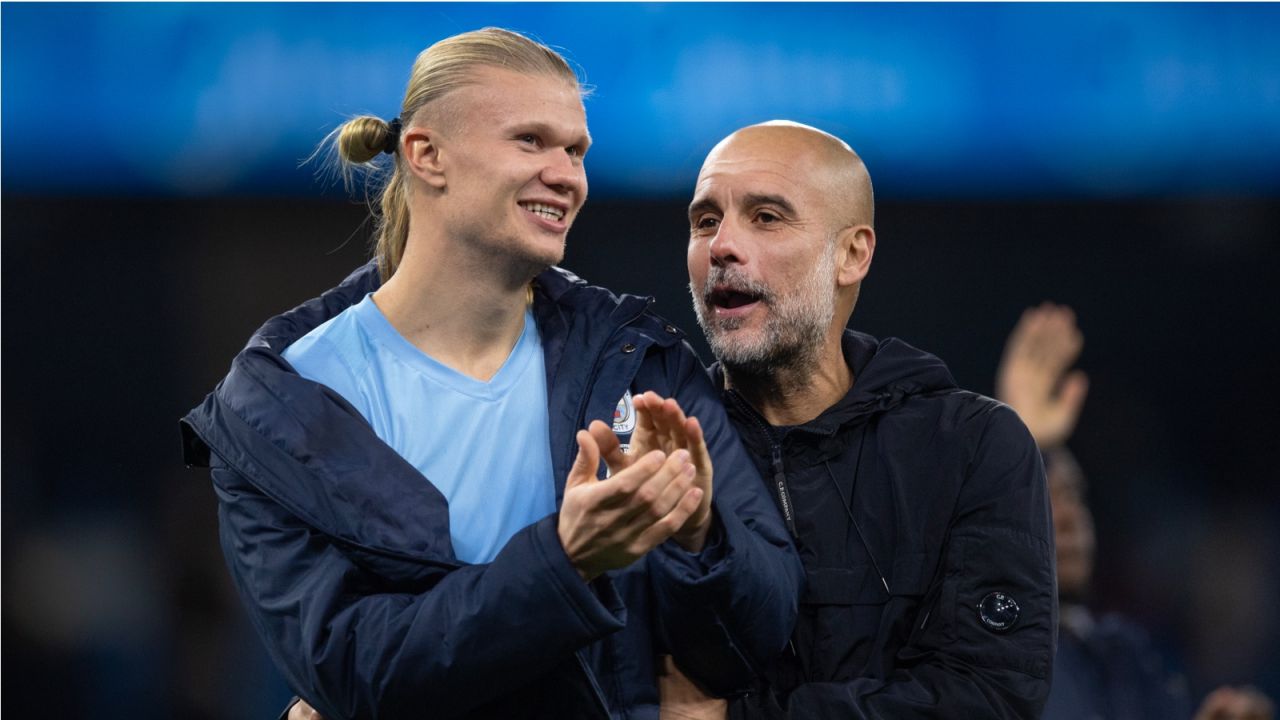 Pep Guardiola, trener Manchesteru City, z krótkimi siwymi włosami i brodą, w ciemnej kurtce, obejmuje ramieniem uśmiechniętego napastnika Erlinga Haalanda, który ma jasny blond kucyk, jasnoniebieską koszulkę i ciemną kurtkę narzuconą na ramiona. Obaj mężczyźni klaszczą na boisku podczas meczu. Guardiola ma świętować swój tysięczny mecz w karierze trenerskiej (fot. Getty).