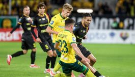 Dynamiczne ujęcie z meczu piłkarskiego GKS Katowice (zawodnik w czarnym stroju z czerwono-żółtymi elementami) kontra Korona Kielce (zawodnik w żółto-zielonym stroju z numerem 23, wykonujący wślizg) w trakcie walki o piłkę na boisku. Mecz ten jest istotny dla GKS Katowice w kontekście walki o oddalenie się od strefy spadkowej oraz dla Korony Kielce, która mimo słabszych wyników utrzymuje wysoką pozycję w ligowej tabeli.